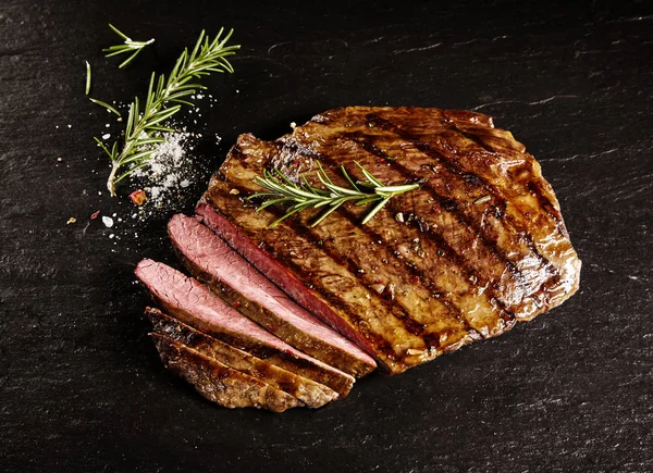 Single roasted medium rare sliced flank beef piece with rosemary over dark table background