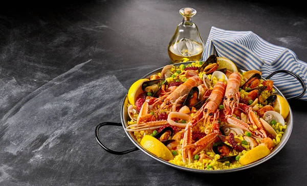 Valencia paella with assorted seafood and shellfish including langoustines, mussels, clams, and squid served with savory seasoned saffron rice and lemon slices, high angle with copy space
