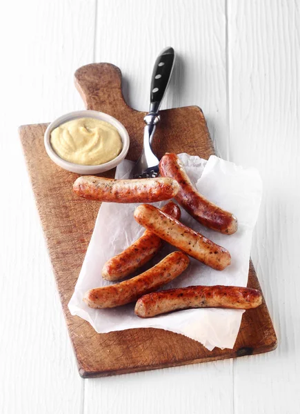 Grilled spicy smoked sausages served on white paper with a mustard dip on a wooden board for a tasty snack