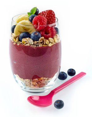Single glass full of mixed acai, banana, blueberry and rolled oats next to pink plastic spoon on white background clipart