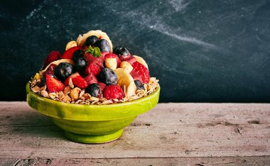 Nutritious giant ceramic green bowl of oats, blueberries, bananas, strawberry on wooden table with copy space and dark background clipart