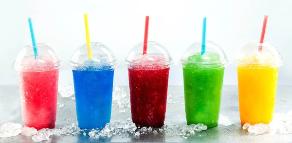 カラフルな冷凍フルーツのパノラマの静物スラッシュグラニータ飲料プラスチック製のテイクアウェイカップ氷と冷たい金属表面上の蓋と飲料ストロー — ストック写真