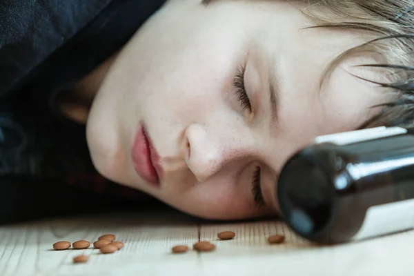 Young boy passed out on drugs and alcohol or dead after committing suicide lying on the floor with an empty medication bottle at his head and capsules around his face
