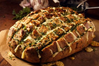 Delicious loaf of party bread stuffed with melted cheese and herbs on brown butcher paper over wooden table clipart