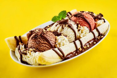 Tropical banana split with chocolate drizzle over three scoops of chocolate, strawberry and vanilla ice cream on fresh bananas, yellow background clipart