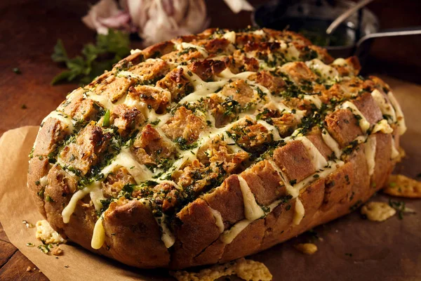 Delicious loaf of party bread stuffed with melted cheese and herbs on brown butcher paper over wooden table