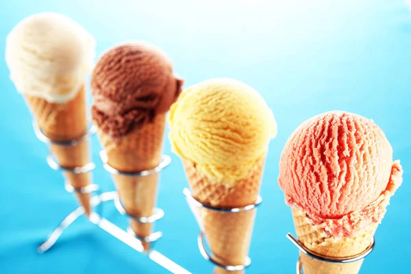 Selective focus view on diagonal row of strawberry, lemon, chocolate and vanilla ice cream cones lined up on stainless steel holder over blue background