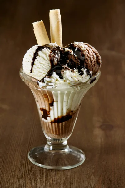 美味的香草和巧克力冰淇淋圣代 配上巧克力酱和薄片饼干 放在木制柜台的高脚杯中 近旁观景 — 图库照片
