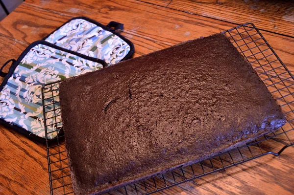 黑巧克力蛋糕坐在冷藏柜上 与五颜六色的烤箱架和海绿色古董碗一起冷却 背景中夹杂着蛋糕 放在老式厨房里那张破旧的木制桌子上 — 图库照片
