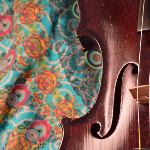 Extreme closeup of violin side against a happy, colorful printed fabric.Violin is an antique from the early 1800's in a dark stain (original finish). Square composition.