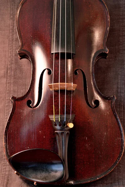古老的小提琴与灰色的缝纫布相抗衡 小提琴是19世纪初的一种带有深色污迹的古董 — 图库照片