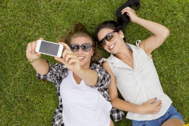 Female best friends lying on the grass and making selfies clipart