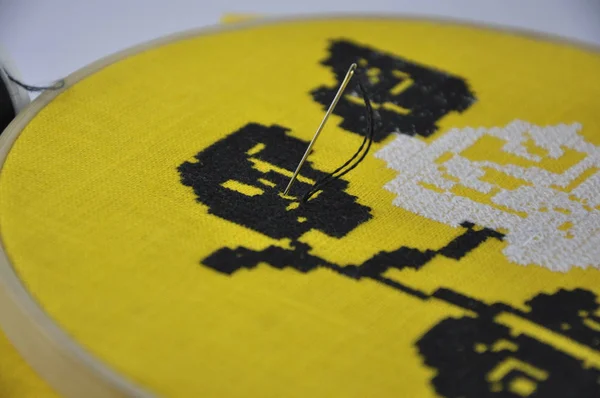 needle with black thread sticks out in yellow cloth in the embroidery