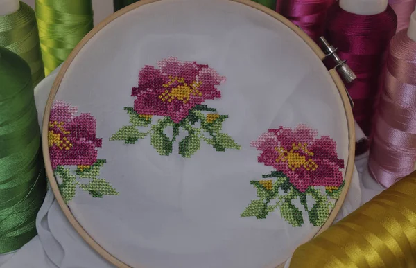 Embroidered cross flowers in wooden hoop on a background thread spools