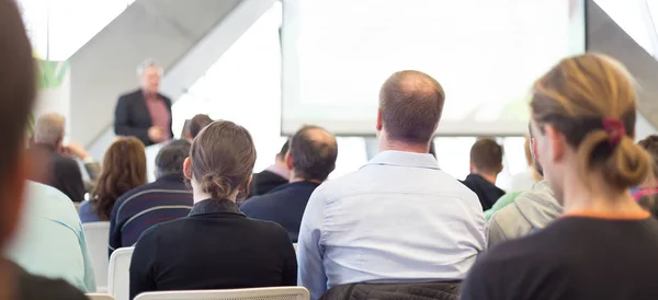 Man giving presentation in lecture hall. Male speeker having talk at public event. Participants listening to lecture. Rear view, focus on people in audience.