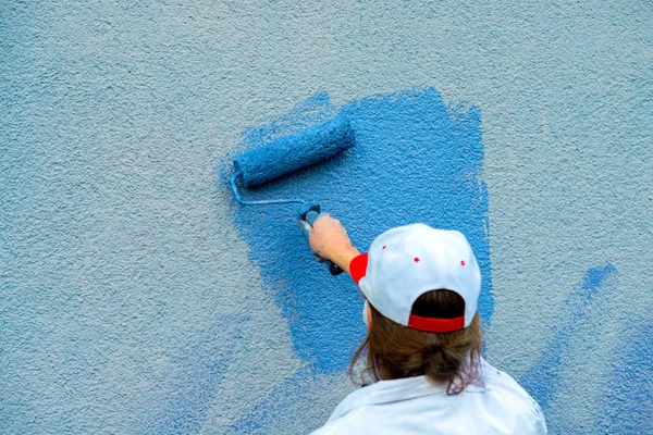 workman painting the wall with paint roller in blue