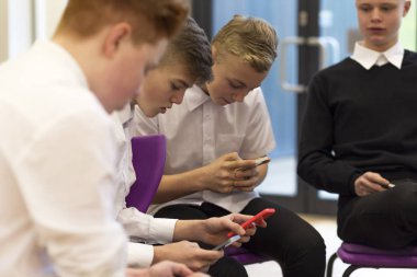 Group of male high school students on their break at school. They are all looking at smartphones. clipart