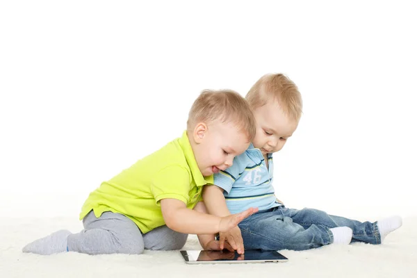 两个拿着电脑平板电脑的小男孩坐在一个白色背景的地板上 — 图库照片