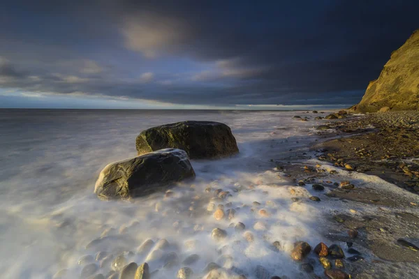 baltic sea in evening light and long exposure,setting sun irradiated branches and stones in sea water troubled sea and foaming waves on the shore,