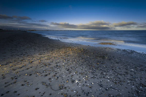 baltic sea in evening light and long exposure,setting sun irradiated branches and stones in sea water,beautiful clouds in a sunset,stormy sea with spume on the beach