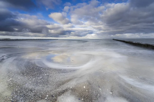 baltic sea in evening light and long exposure,setting sun irradiated branches and stones in sea water troubled sea and foaming waves on the shore,