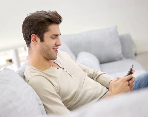 Lächelnder Gutaussehender Mann Sitzt Mit Smartphone Auf Couch — Stockfoto