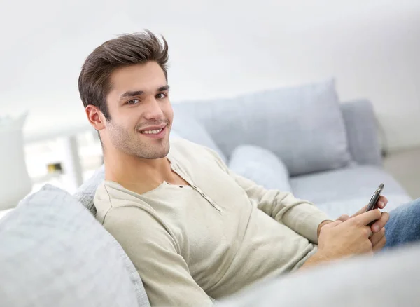 Lächelnder Gutaussehender Mann Sitzt Mit Smartphone Auf Couch — Stockfoto