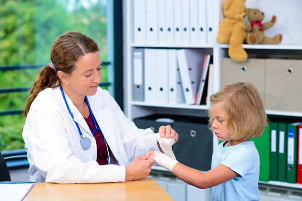 穿着白色实验室外套的女儿科医生用绷带包扎一个小女孩的胳膊 — 图库照片