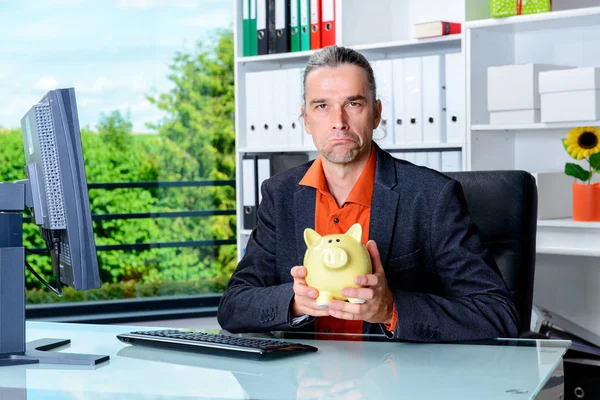 young angry business man at his desk with piggy bank