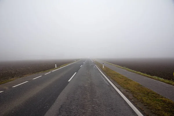 霧の中の農村部を通る車のない道路 — ストック写真