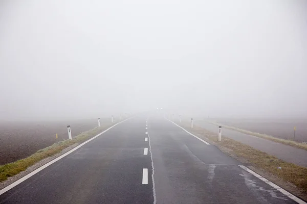 霧の中の農村部を通る車のない道路 — ストック写真