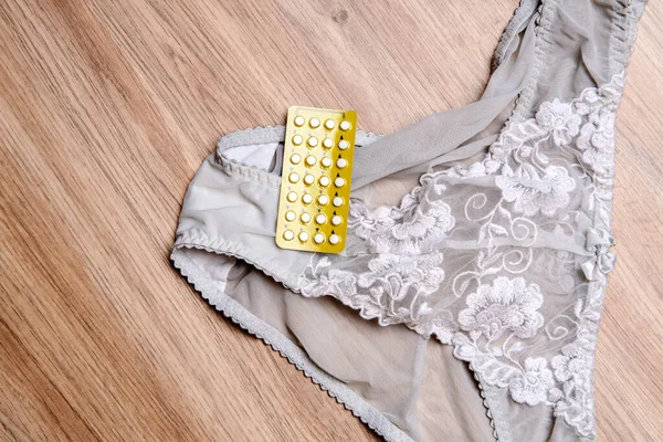 womans panties with birth control pill on wooden floor