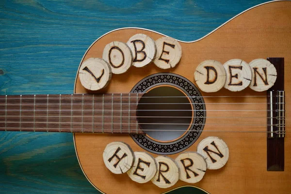 guitar on blue green wood with individual wooden discs on which the words form praise the lord