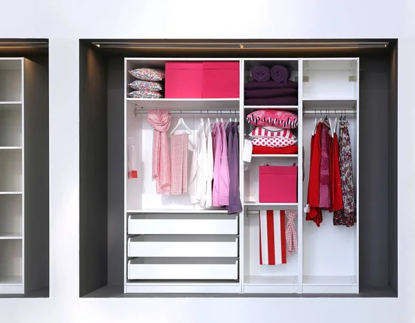 Inside open closet with female clothes and accessories in pink colour scheme