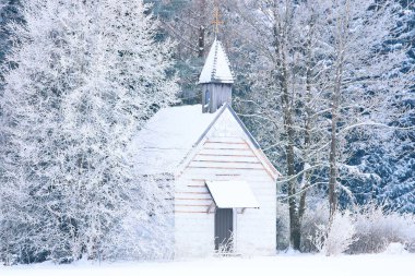 Small woody chapel in frozen snowy forest. Stock photo captured in Bavarian Alpine rural region Allgaeu. clipart