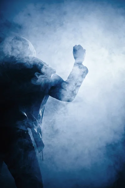 一个穿着皮夹克的人的拳头和手 在薄雾中对着光的帽衫 — 图库照片
