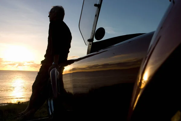 Older Man views sunset from car bonnet