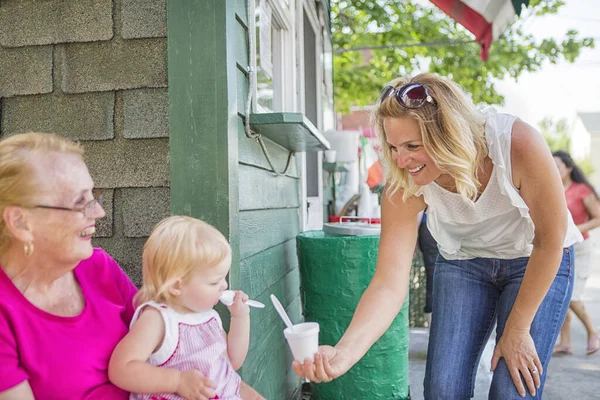 Ice cream parlour shop keeper handing ice cream to baby girl and her grandmother