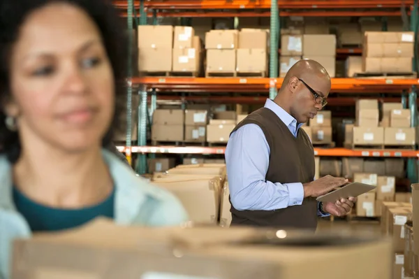 Male warehouse manager using digital tablet, woman in foreground