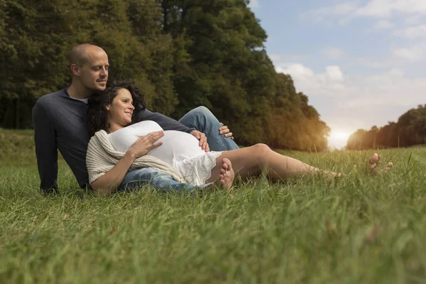 妊娠中の夫婦は公園で草の上に座って — ストック写真