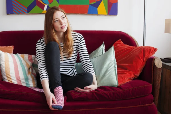 Young woman sitting on sofa with feet up