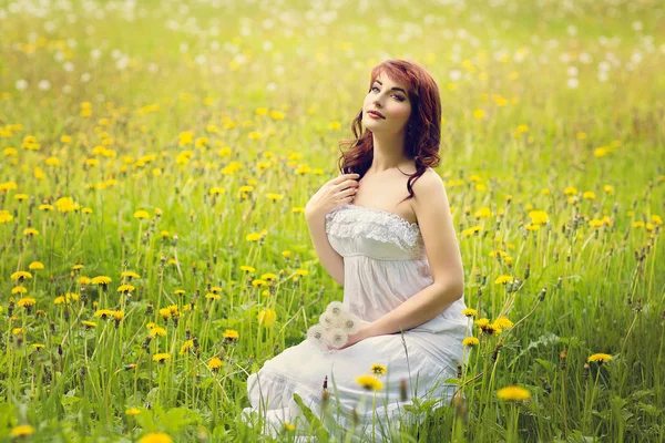 タンポポの花の分野で白い長いドレスに座って美しい若い女性 屋外撮影 — ストック写真