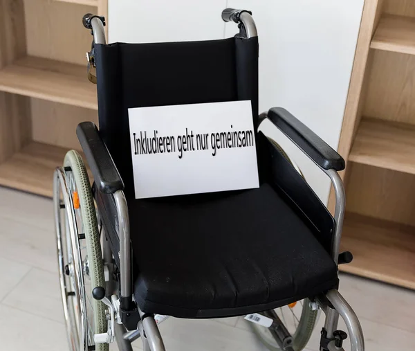空荡荡的轮椅面对着墙体 轮椅上的标志表明 只有通过共同努力才能融入社会 — 图库照片