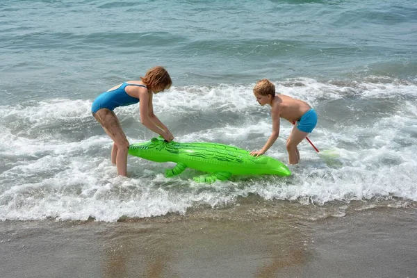 一个男孩和一个女孩在一个有鳄鱼气垫的海滩上玩耍 — 图库照片