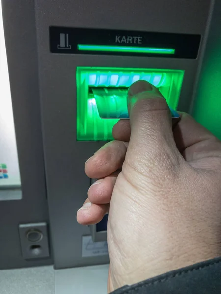 Entering the bank card at an ATM at dusk that is lighted green.