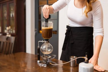 equipment, coffee shop, people and technology concept - close up of woman stirring coffee grounds in siphon coffeemaker top vessel at cafe bar or restaurant kitchen clipart