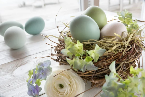 Pastel Renkli Paskalya Yumurtalarıyla Saman Yuvasındaki Çiçekler Beyaz Ahşap Bir — Stok fotoğraf
