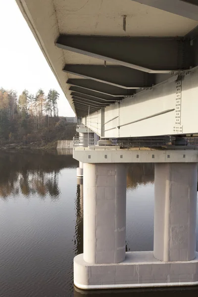 new bridge across the river, made of concrete and metal. The photo was taken close-up with the bottom of the structure, visible columns and the river. Autumn season