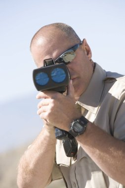 Mature traffic officer looking through radar gun clipart