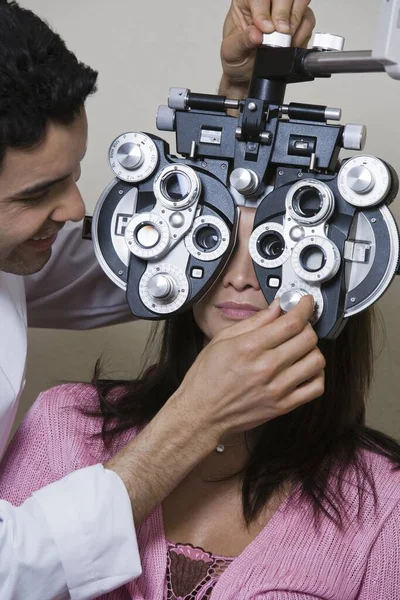 Glücklicher Optometrist Der Phoropterpaneele Einstellt Während Patientin Vor Grauem Hintergrund — Stockfoto